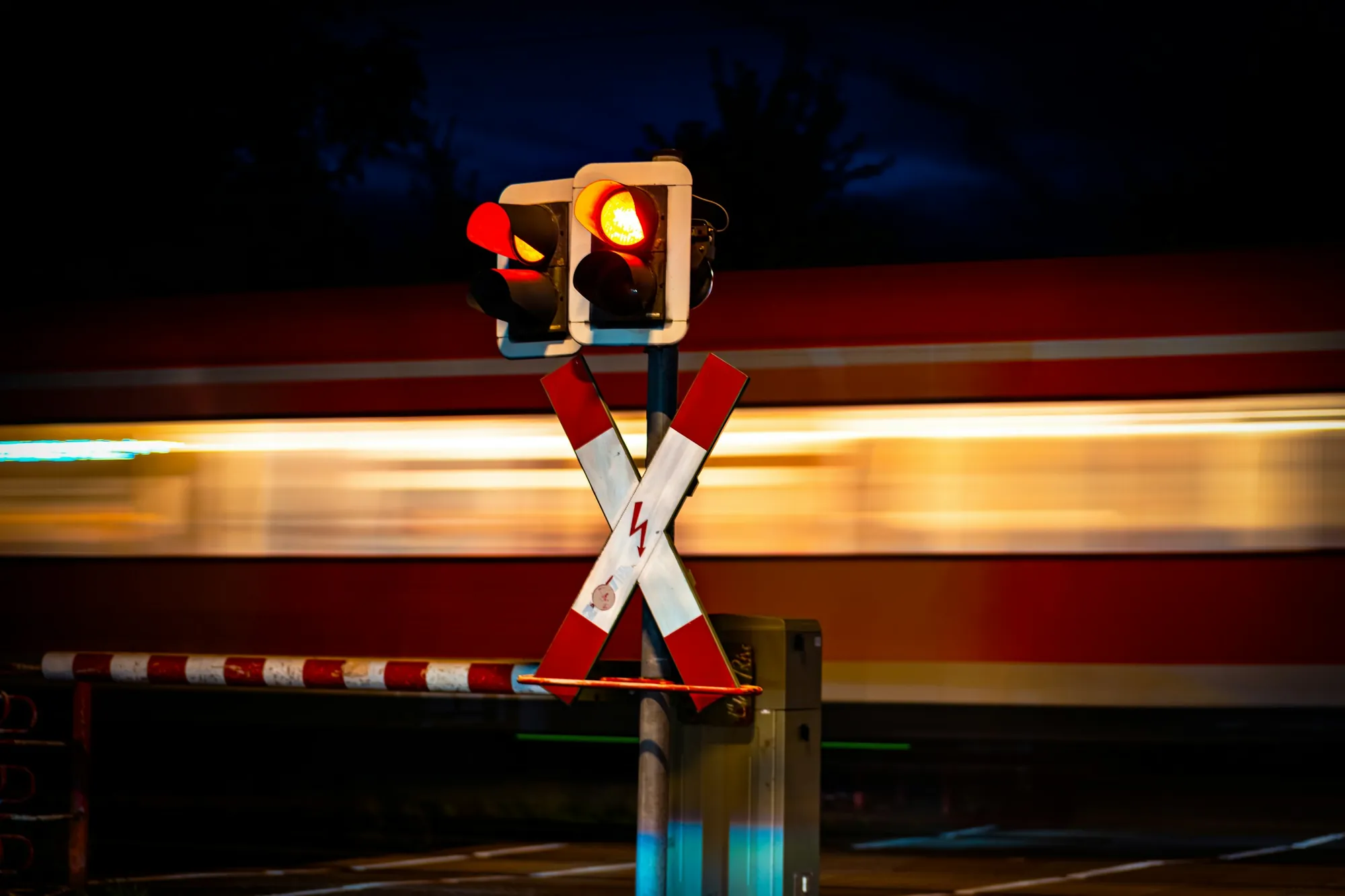 Zug fährt nachts an einem Bahnübergang mit rotem Blinklicht vorbei